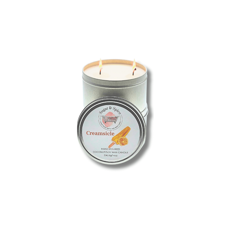 A silver-colored, metal tin container with a lid, containing a two-wick Creamsicle-scented coconut wax candle. The label on the tin has orange and white colors and text.