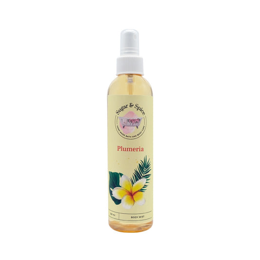 A bottle of Plumeria Body Mist with a white spray nozzle. The label features the name 'Plumeria' and an illustration of a plumeria flower with green leaves.
